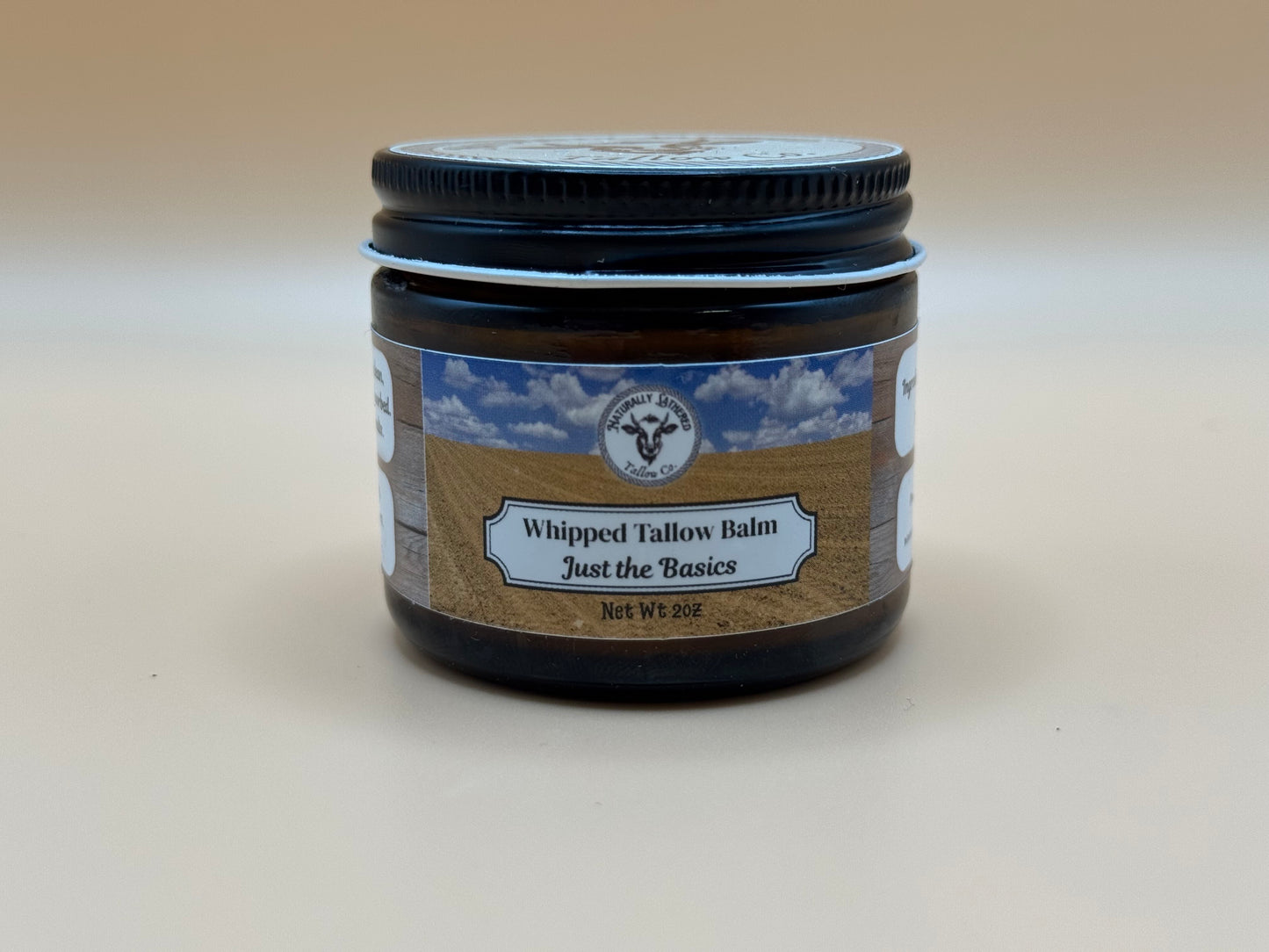 Jar of whipped tallow balm with a label on a beige background